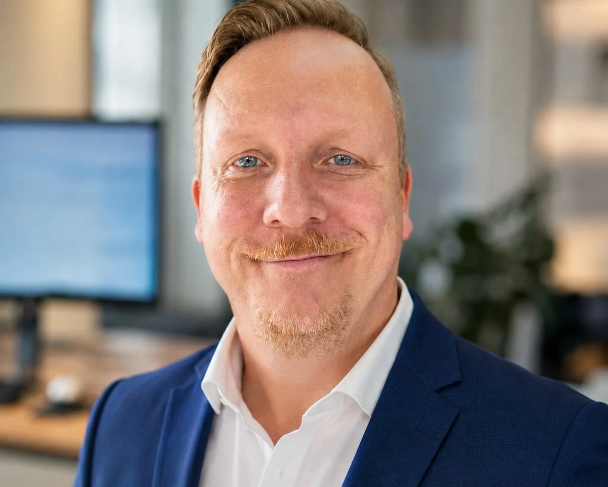 Porträt von René Stiegler, KI-Sparringspartner aus Nordhessen, im blauen Sakko vor seinem Arbeitsplatz. Das Foto wurde mit KI bearbeitet.
